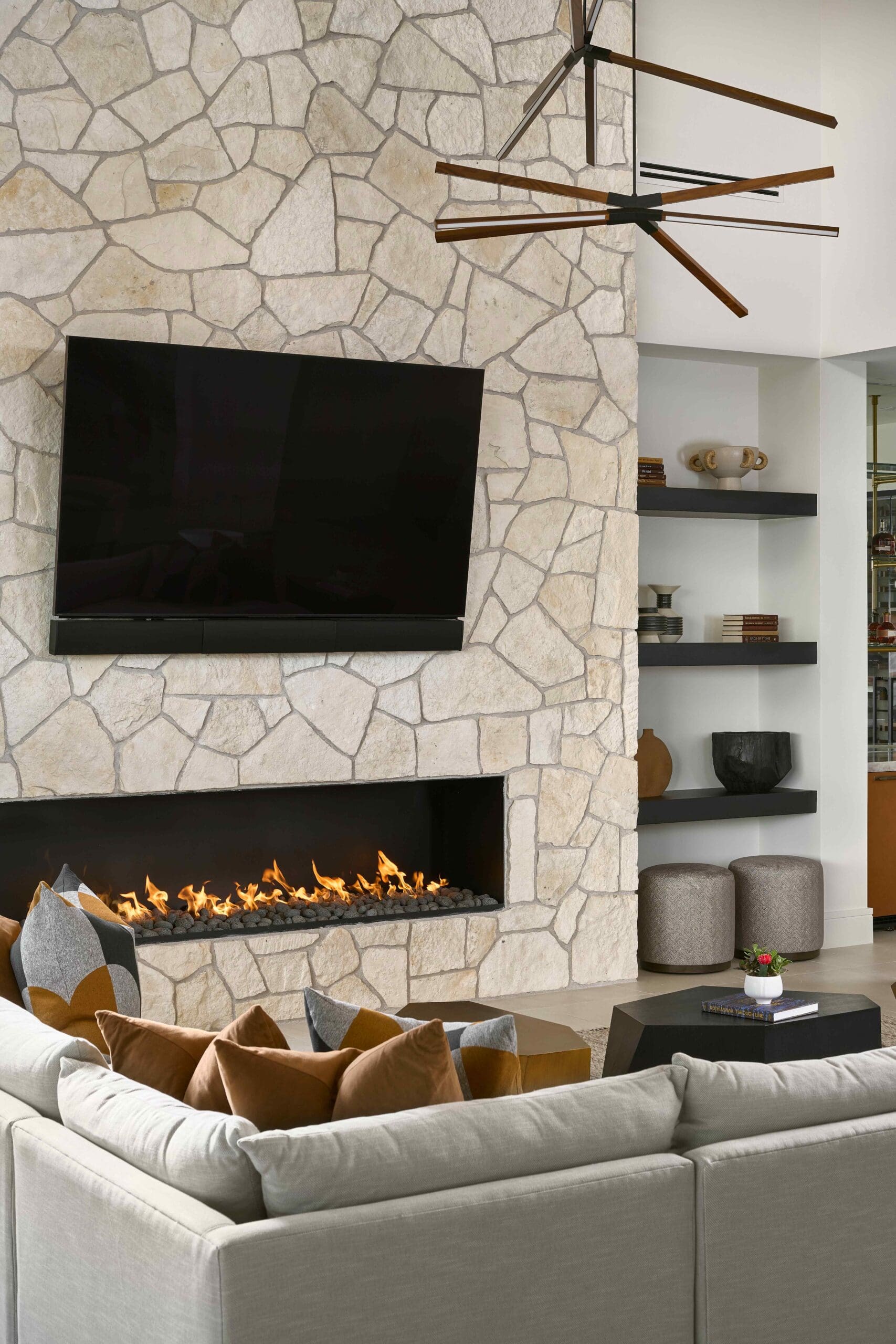 Stone fireplace wall with integrated television and sculptural lighting by JSF Design